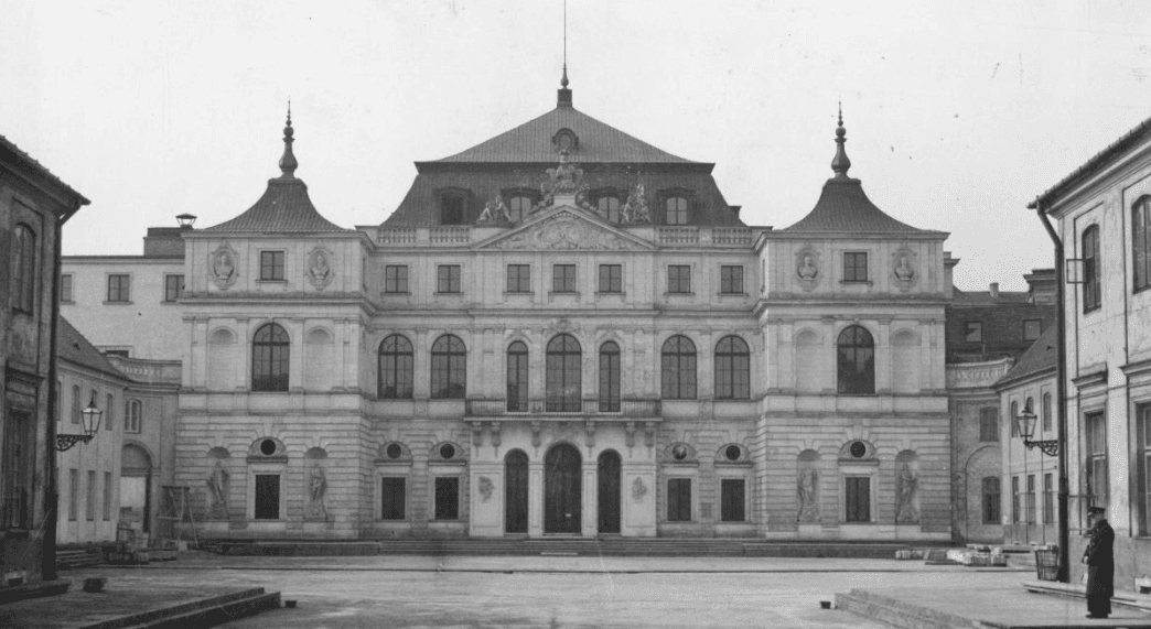 Czarno-białe zdjęcie fasady dwupiętrowego pałacyku z ozdobnym wejście. 